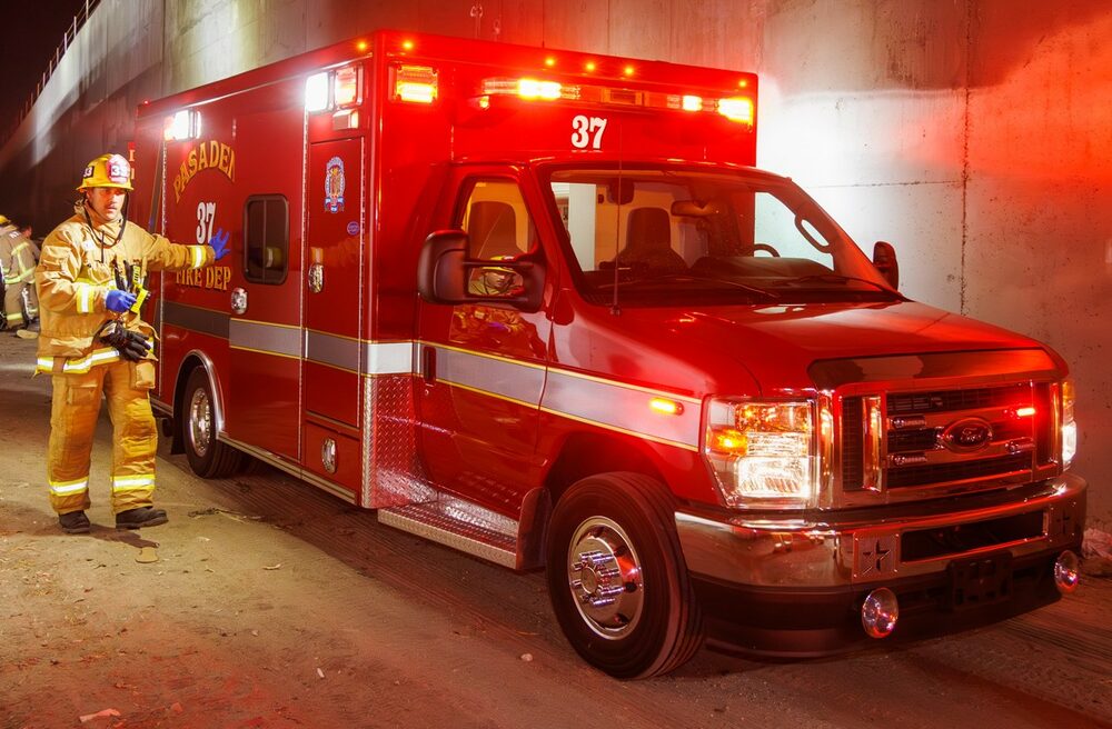 A firefighter beside Pasadena Fire Department Rescue Ambulance 37 at night