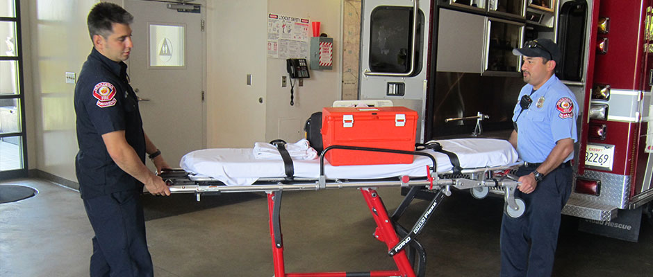 Two EMS Reserve members moving a gurney in the fire station apparatus bay